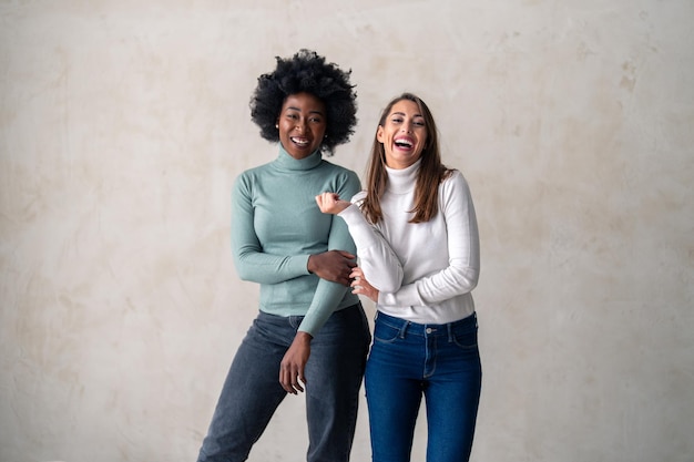 Mulheres jovens de diferentes etnias sorrindo felizes enquanto estão juntas contra o fundo de um estúdio