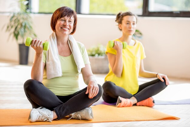 Mulheres jovens e mais velhas em roupas esportivas, sentadas durante o treinamento de ioga em ambientes fechados