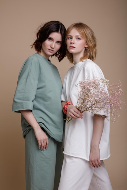 mulheres jovens elegantes em terno esportivo branco e verde menta, estilo de caminhada, tamanho grande posando em marrom