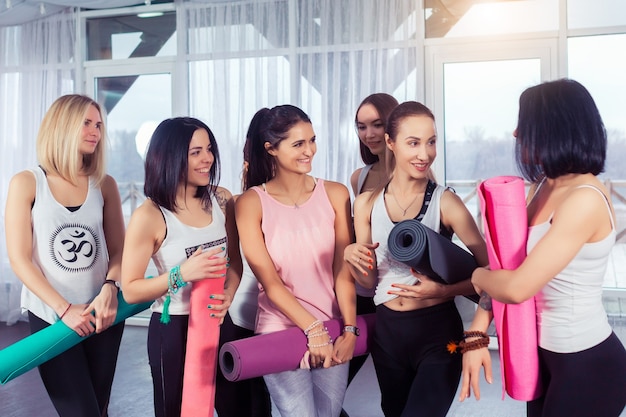 Mulheres jovens na aula de ioga sorrindo e conversando após a prática de fitness com esteiras de ioga