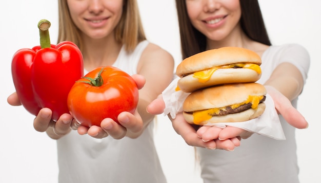 Mulheres jovens segurando legumes e hambúrguer