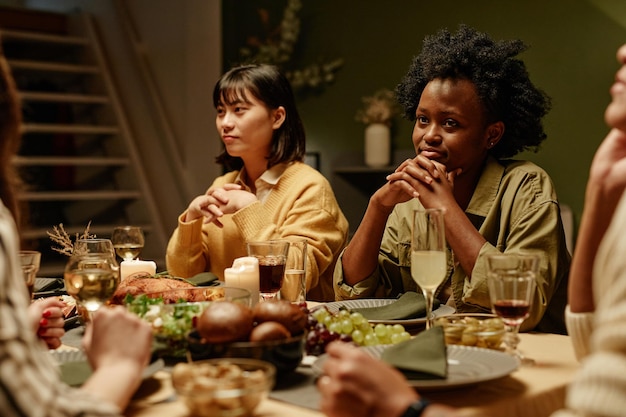 Mulheres jovens sentadas à mesa de jantar e ouvindo amigos enquanto comemoram algo em casa