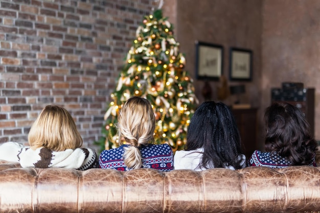 Mulheres jovens sentadas no sofá perto da árvore de Natal em um loft aconchegante