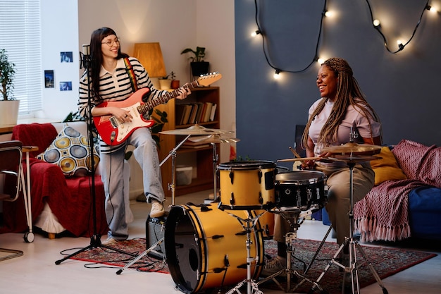 Mulheres jovens tocando guitarra e bateria juntas no estúdio durante a repetição