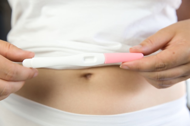 Mulheres jovens vestindo cueca branca com a mão segurando o teste de gravidez em branco e a barriga. closeup cópia espaço