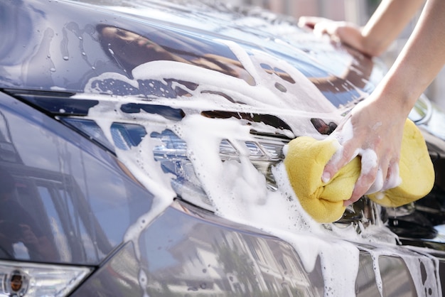 Mulheres lavando um carro cinza e sabão com uma esponja amarela.