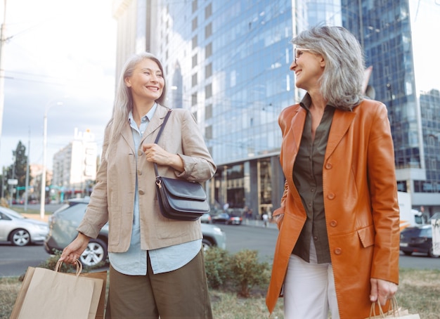 Mulheres maduras felizes com sacolas de compras caminhando pela rua da cidade moderna