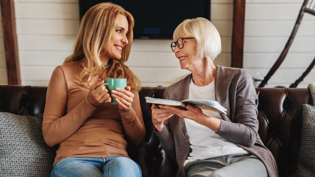 Mulheres maduras lendo livro com sua filha tomando café em casa