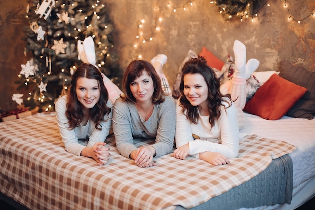 Mulheres morenas atraentes - mãe e suas duas filhas adolescentes de pijama, deitadas na cama olhando para a frente