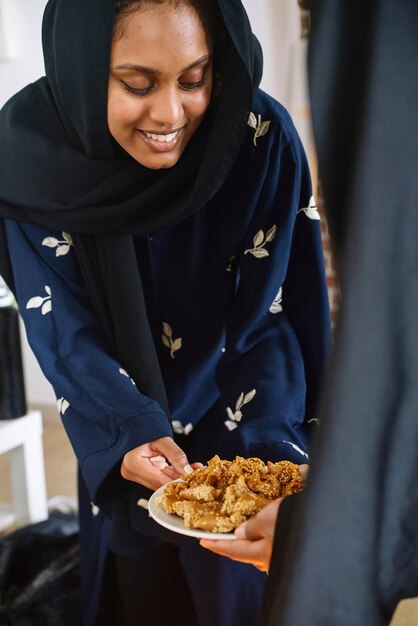 Mulheres muçulmanas vestindo abayas presenteando e compartilhando doces árabes durante o Ramadã