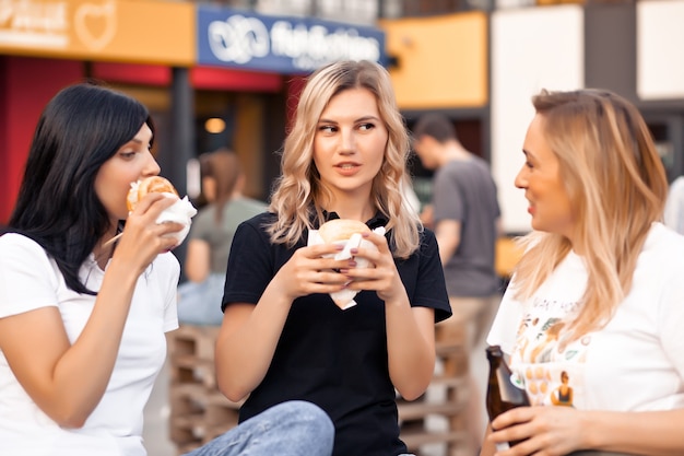 Mulheres muito jovens comendo hambúrguer ao ar livre na rua.