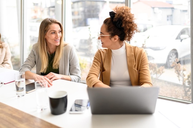 Mulheres profissionais sorridente com laptop discutindo ideias e estratégias em sala de reuniões moderna