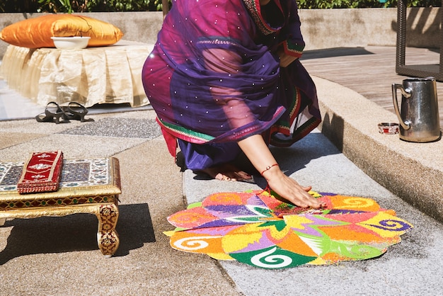 Mulheres que decoram a arte tradicional do arroz (Rangoli) no assoalho para o casamento indiano