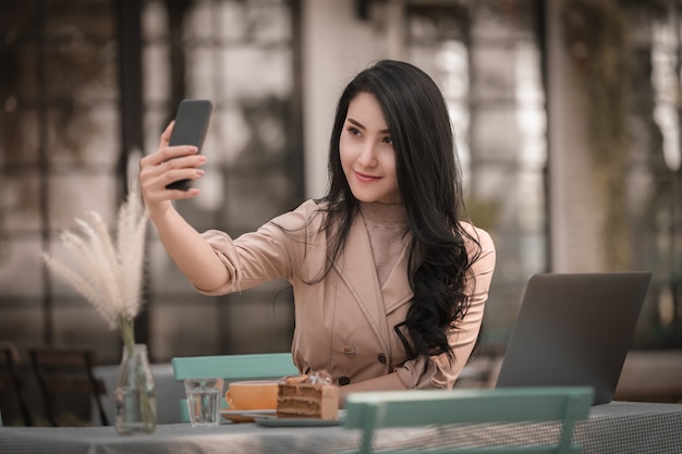 Mulheres sentadas relaxantes selfie e sorrindo no smartphone e laptop em cima da mesa