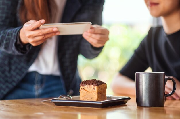 Mulheres usando celular para tirar uma foto de bolo e café antes de comer no café