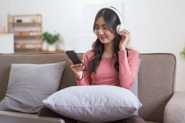 Mulheres usando fone de ouvido para ouvir música no smartphone enquanto relaxam no sofá no estilo de vida em casa