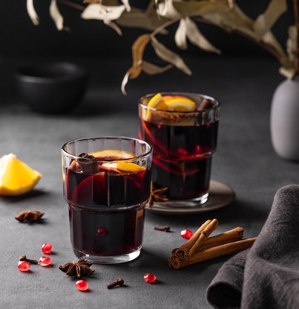 Foto mulled-wein mit orange, apfel, granatapfel und zimt in gläsern auf dunklem hintergrund das konzept eines traditionellen warmen wintergetränks mit gewürzen und früchten