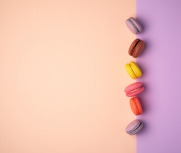 Multi farbige macarons mit sahne auf einem purpurroten beige hintergrund, flache lage