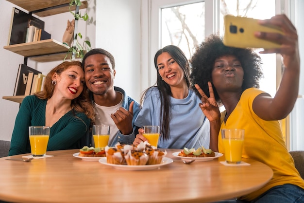 Multiethnische Freunde bei einem Frühstück mit Orangensaft und Muffins zu Hause selfie lächelnd