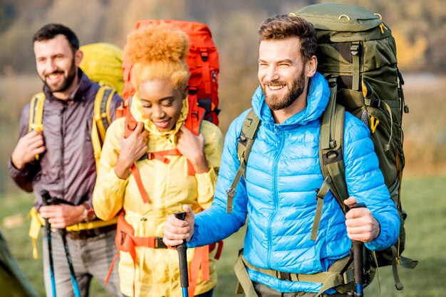 Multiethnische Freunde in bunten Jacken beim Wandern mit Rucksäcken im Wald