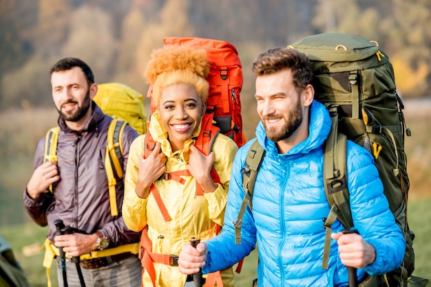 Multiethnische Freunde in bunten Jacken beim Wandern mit Rucksäcken im Wald