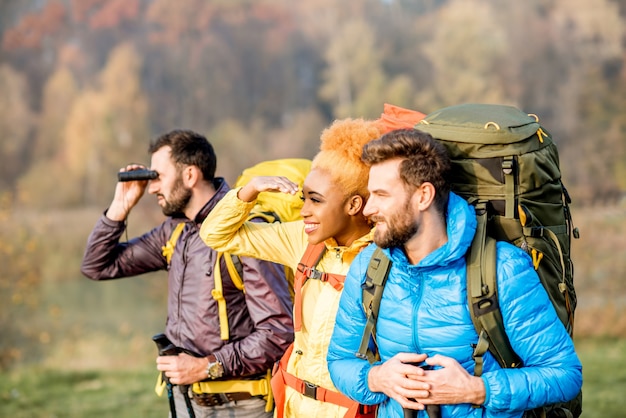 Multiethnische Freunde in bunten Jacken beim Wandern mit Rucksäcken im Wald