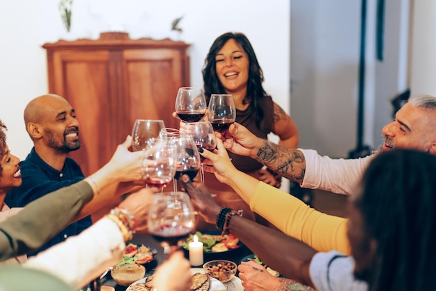 Multiethnische Freunde sitzen beim Abendessen zusammen, feiern und stoßen mit Wein an