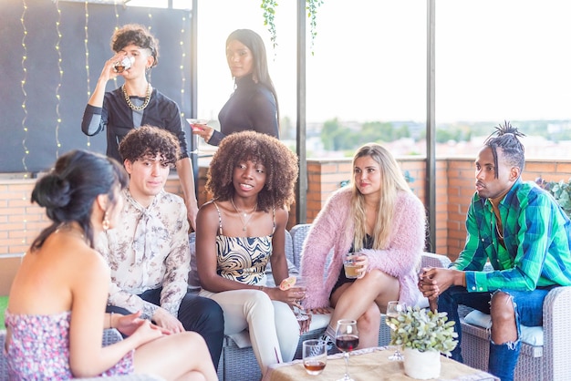 Multiethnische Freunde unterhalten sich auf einer Terrasse, während sie tagsüber etwas trinken.