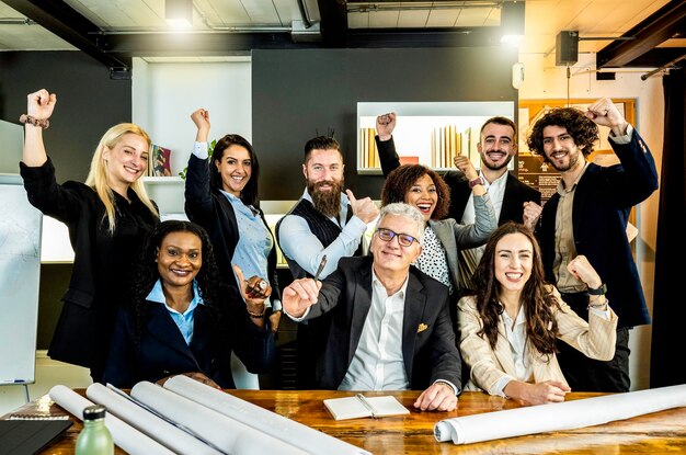 Multiethnische fröhliche Geschäftsleute, die in der Unternehmenszentrale für ein Gruppenfoto in die Kamera schauen, während sie gemeinsam an einem nachhaltigen Innovationsprojekt arbeiten Zielerreichungskonzept