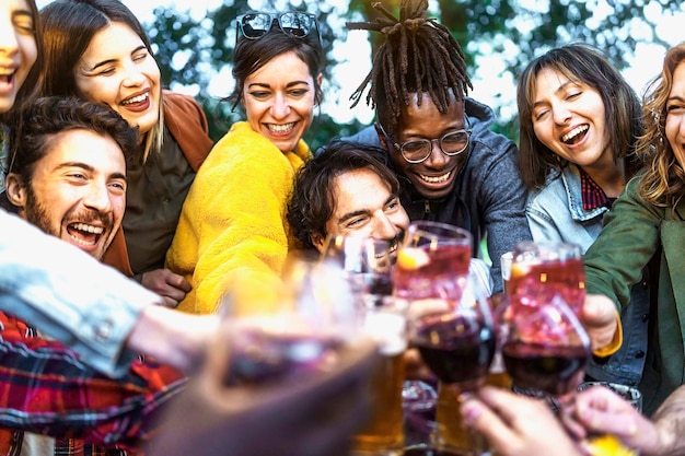 Foto multiethnische gruppe aufgeregter junger leute, die spaß daran haben, gemeinsam wein und bier auf der terrasse anzustoßen