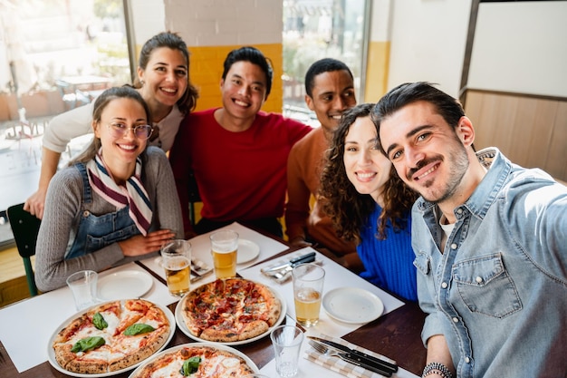 Multiethnische Gruppe macht ein Selfie-Foto in einem Restaurant, während sie Pizza mit fröhlichem Gesichtsausdruck isst