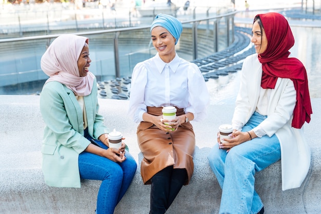 Multiethnische Gruppe muslimischer Mädchen, die Freizeitkleidung und traditionelle Hijab-Bindung tragen und Spaß im Freien haben - 3 arabische junge Mädchen