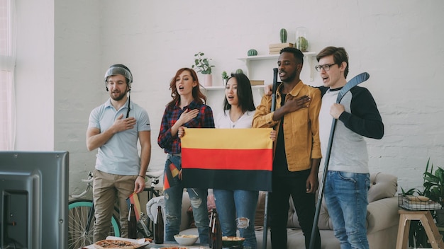 Multiethnische Gruppe von Freunden, die die deutsche Nationalhymne hören und singen, bevor sie Sport treiben