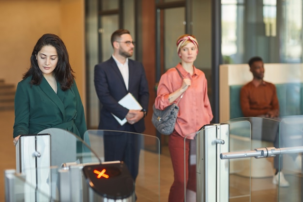 Multiethnische Gruppe von Menschen, die beim Betreten des Bürogebäudes ein automatisiertes Tor passieren, konzentrieren sich auf junge Frauen aus dem Nahen Osten, die ihren Personalausweis klauen, und kopieren Platz