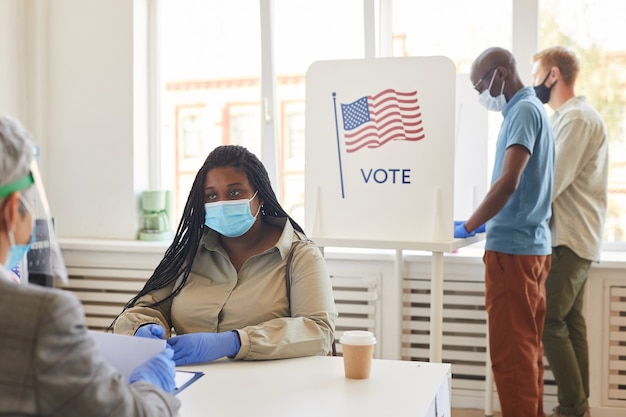 Multiethnische Gruppe von Menschen, die Masken tragen, die am Wahltag nach der Pandemie im Wahllokal abstimmen
