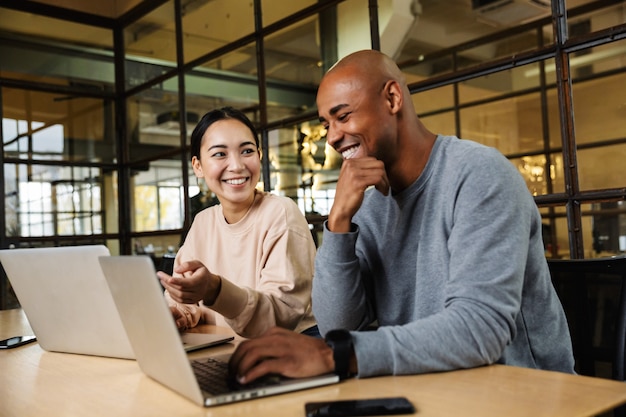 Multiethnische junge weibliche und männliche Mitarbeiter, die am Tisch sitzen und im Büro an Laptops arbeiten