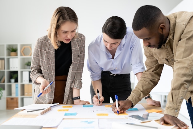 Multiethnische Marketing-Spezialisten stehen am Tisch und fügen neue Ideen in die kreative Plan-Tafel ein