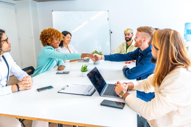 Multiethnische Menschen schütteln sich die Hände und sitzen in einem Coworking-Raum