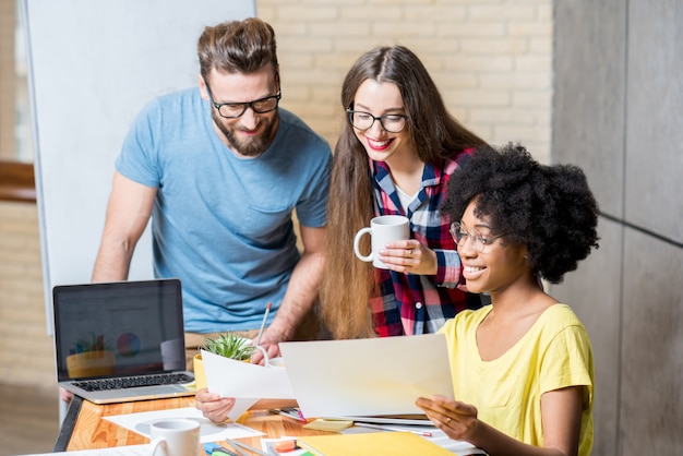 Multiethnische Mitarbeiter, die lässig in bunten Kleidern gekleidet sind und während des Meetings im Büro mit Laptop und Dokumenten arbeiten