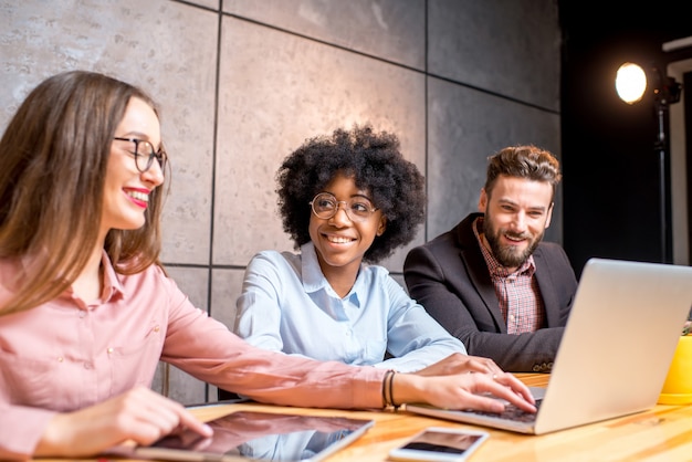 Foto multiethnische mitarbeiter, die mit gadgets im modernen bürointerieur auf dem grauen wandhintergrund zusammenarbeiten