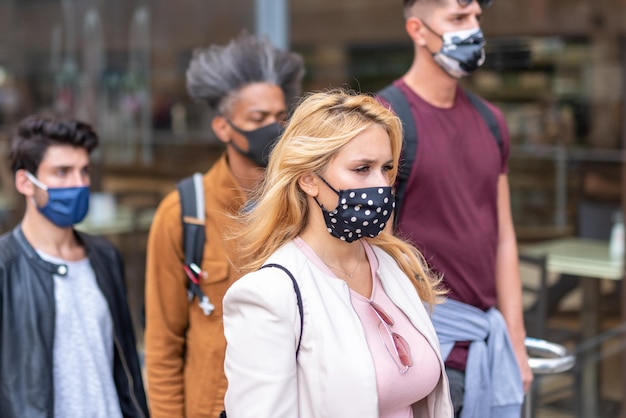 Foto multiethnische städtische menge junger menschen, die mit einer gesichtsmaske durch die straßen gehen, konzentrieren sich auf den traurigen und besorgten blick einer blonden frau, die die neue normale lebensweise der stadt sozial distanziert