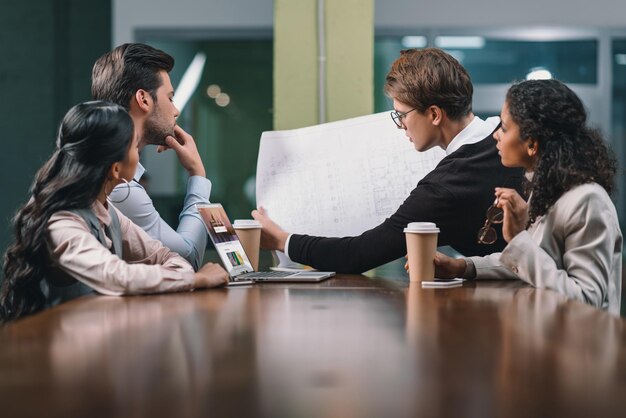 Multiethnisches Geschäftsteam, das beim Treffen mit Blaupausen arbeitet