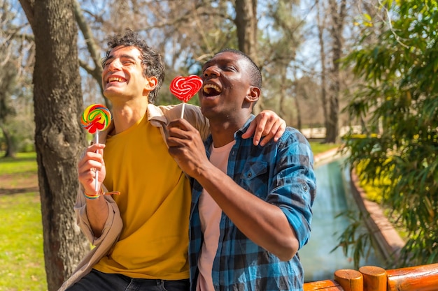 Multiethnisches männliches Paar, das lächelnd ein Lollipop-LGBT-Konzept isst