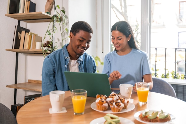 Multiethnisches Paar, das beim Frühstück online mit dem Computer einkauft