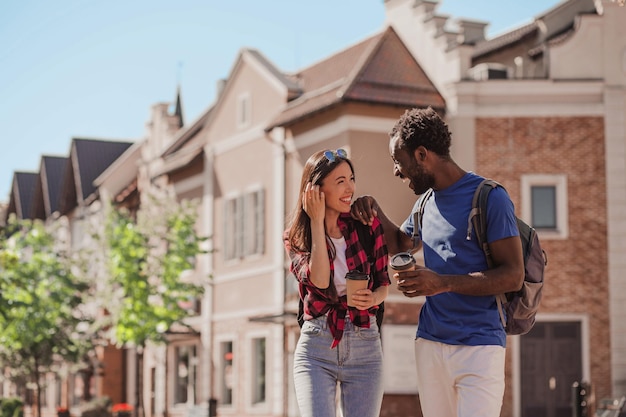 Multiethnisches Paar spricht zusammen und hält Kaffeetassen auf der Straße