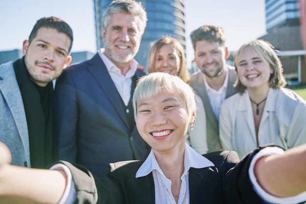 Multikulturelle Gemeinschaft von Menschen, die zusammen vor der Kamera lächeln, glückliche, vielfältige Geschäftsleute, die ein Selfie mit einem intelligenten Mobiltelefon machen, Freundschaft und das Konzept der menschlichen Beziehung