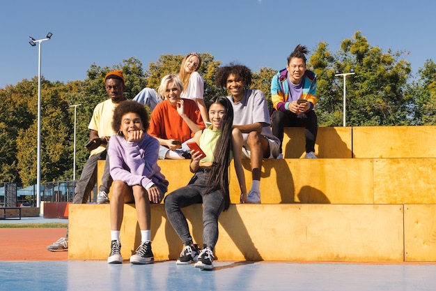 Multikulturelle Gruppe junger Freunde, die sich im Freien verbinden und Spaß haben - Stilvolle, coole Teenager, die sich im urbanen Skatepark versammeln