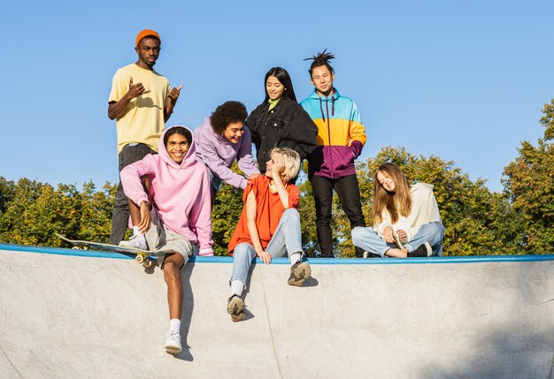 Multikulturelle Gruppe junger Freunde, die sich im Freien verbinden und Spaß haben - Stilvolle, coole Teenager, die sich im urbanen Skatepark versammeln