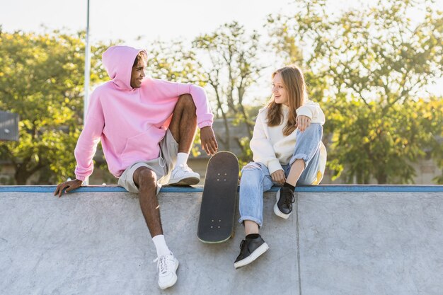 Multikulturelle Gruppe junger Freunde, die sich im Freien verbinden und Spaß haben - Stilvolle, coole Teenager, die sich im urbanen Skatepark versammeln