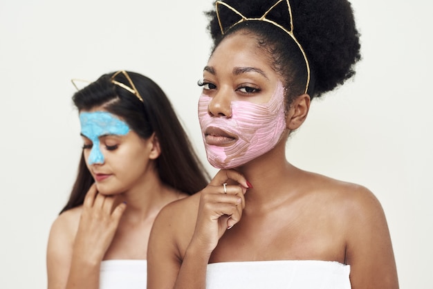 Multimasking. Duas garotas étnicas diferentes estão se abraçando. Os rostos das meninas estão cobertos com máscaras